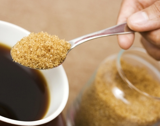 Adding a spoonful of brown sugar into a cup of coffee