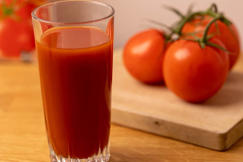 Glass of tomato juice and tomatoes in the background