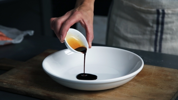 Pouring balsamic vinegar into a white bowl