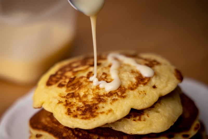 Pouring condensed milk over pancakes