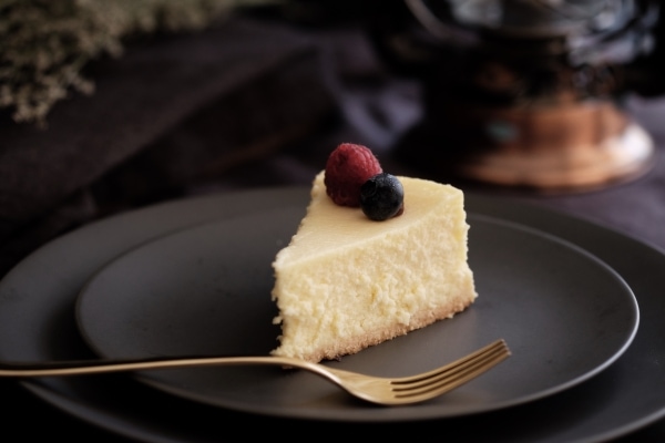 Slice of fruit-garnished cheesecake on a black plate